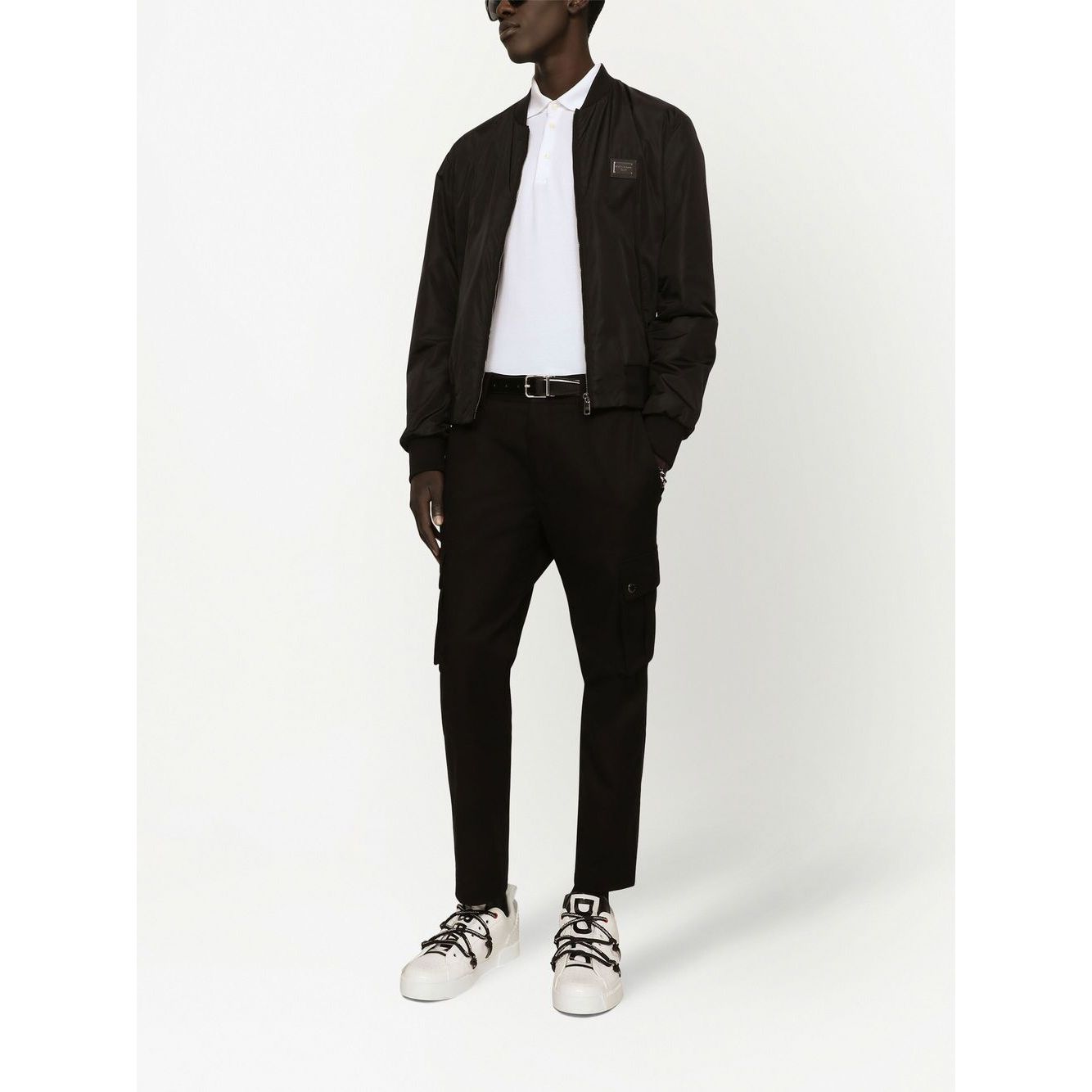 Model wearing Dolce & Gabbana Logo cotton polo shirt with black jacket and pants, showcasing white sporty shoes.