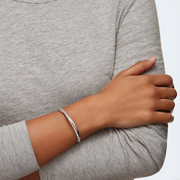 Person wearing a simple silver bracelet on their wrist over a gray long-sleeve shirt.