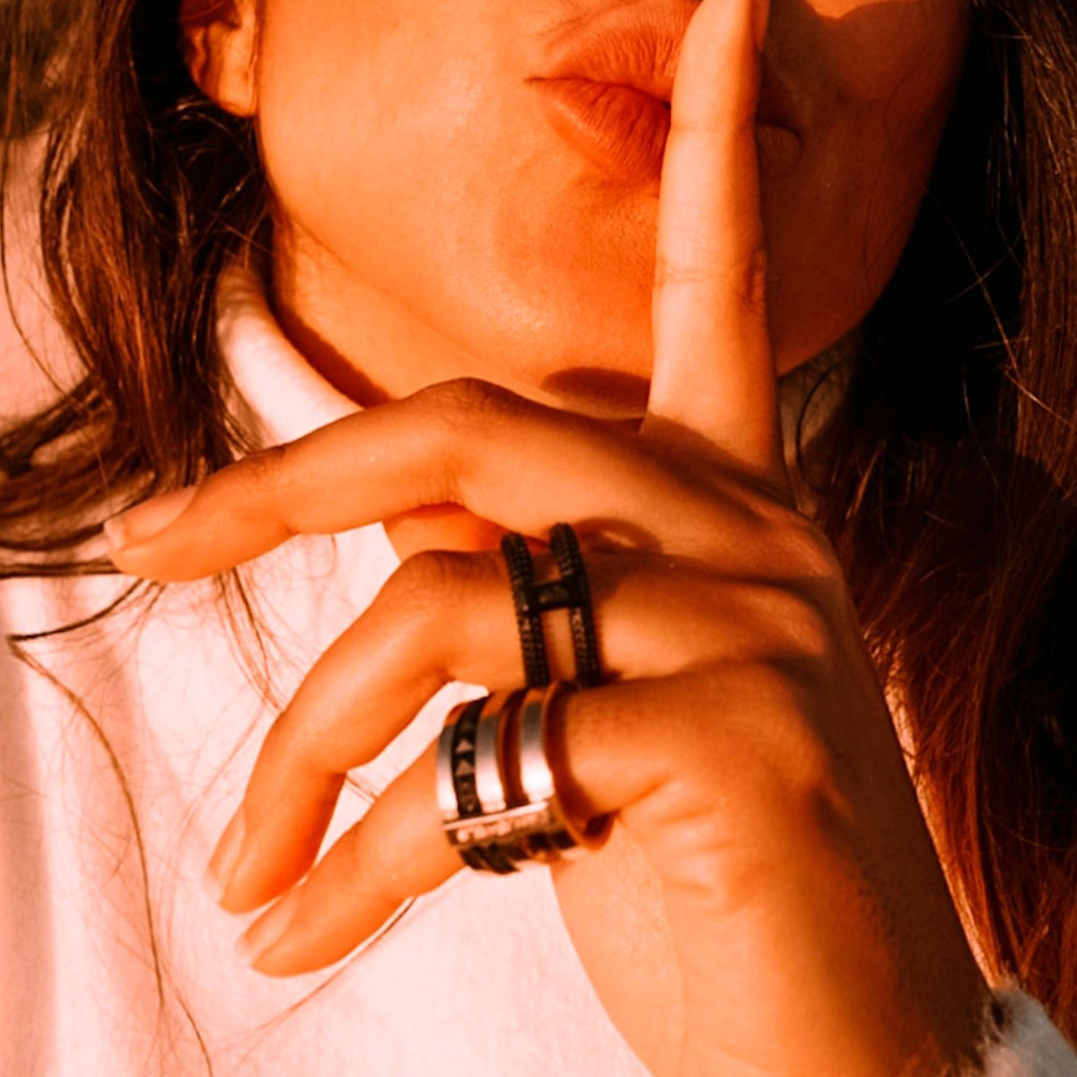 Close-up of woman wearing AN JEWELS JEWELRY Mod. AR.R2NS02BK-8 ring, gesturing silence with finger on lips in warm sunlight