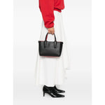 Person holding a black Christian Louboutin Cabata mini leather tote bag with spiked studs, featuring top handles and a red interior.