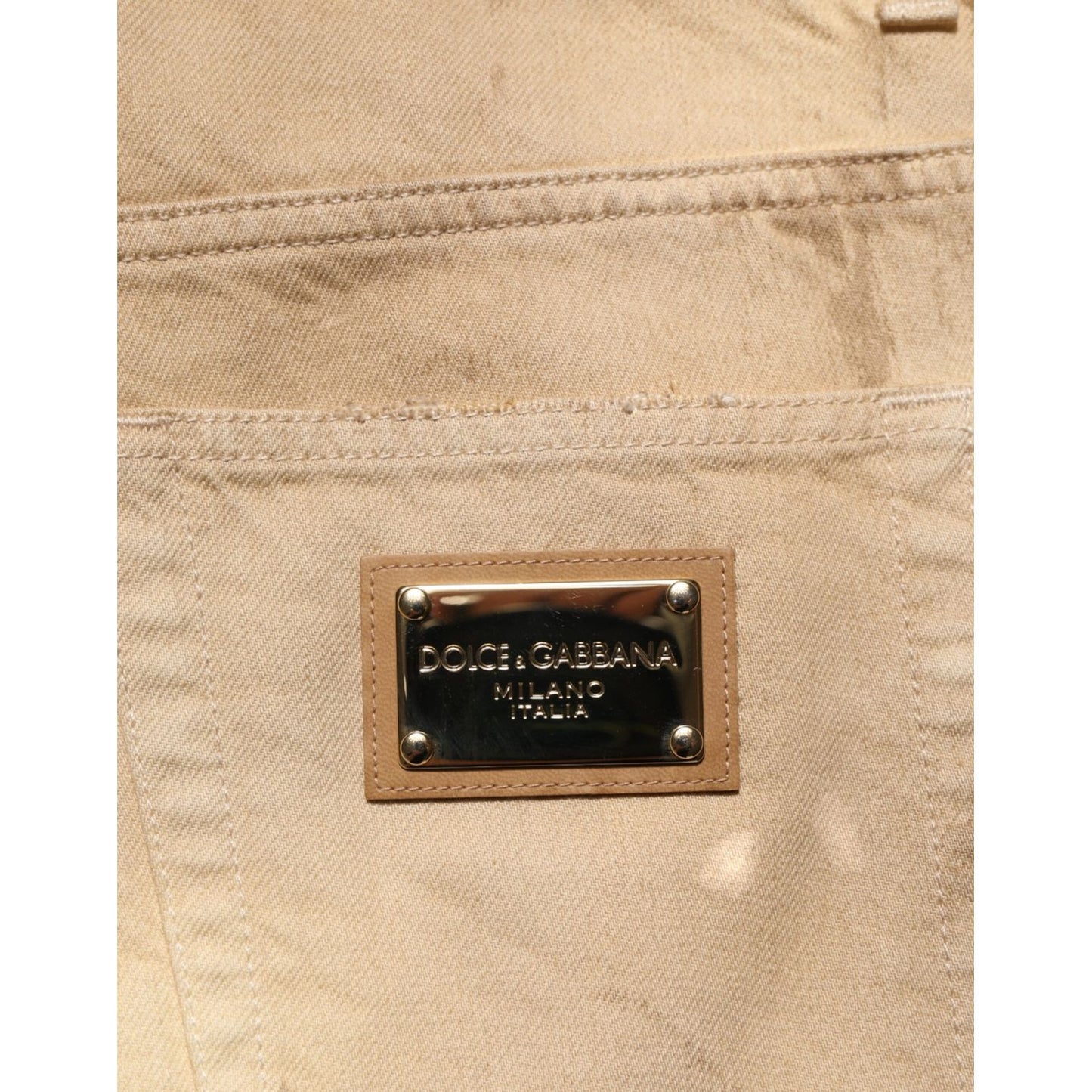 Close-up of Dolce & Gabbana Beige Cotton Loose Tattered Men Denim Jeans with brand label on beige fabric.