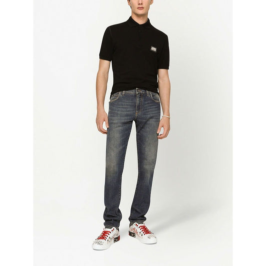 Model wearing a Dolce & Gabbana Logo cotton polo shirt in black with silver-tone logo plaque, paired with jeans and sneakers.
