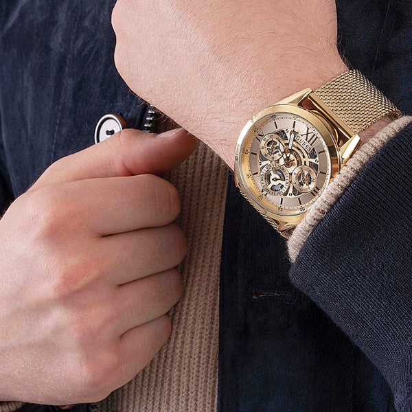 Alt Tag: Person wearing a stylish golden watch, featuring the intricate design of GUESS Mod. TAILOR.